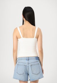 Valge vormi kohandatud tank top, millel on paksud õlavarre rihmad, koos helesiniste denim lühikesed pükstega, millel on taga taskud ja räbaldunud servad.