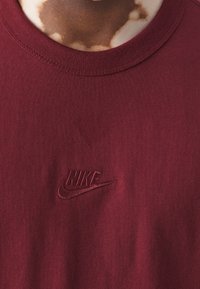 Bordový nike tričko vyrobené z bavlny s kulatým výstřihem, s vyšitým logem v tmavším odstínu, hladká textilie.