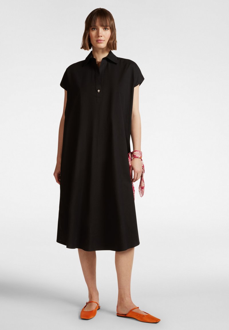 Robe chemise noire à manches courtes avec un col et des détails de boutons. Tissu lisse, longueur genou, assortie à des chaussures orange et un accessoire à motifs roses.