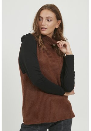 Brauner gerippter Strick-Ärmelloser Pullover mit hohem Kragen, kombiniert mit einem schwarzen Langarmoberteil. Seitenschlitze am Saum sichtbar.