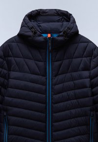 Jūras spēku pufēta jaka ar quilted dizainu, ar kapuci, ziliem rāvējslēdzēju akcentiem un regulējamiem trošu savilcējiem. Gluda, spīdīga auduma tekstūra.