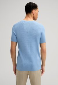 Pullover blu chiaro a maniche corte con tessuto a maglia testurizzato e polsini a coste. Presenta un colletto a giro e una linea dell'orlo dritta.