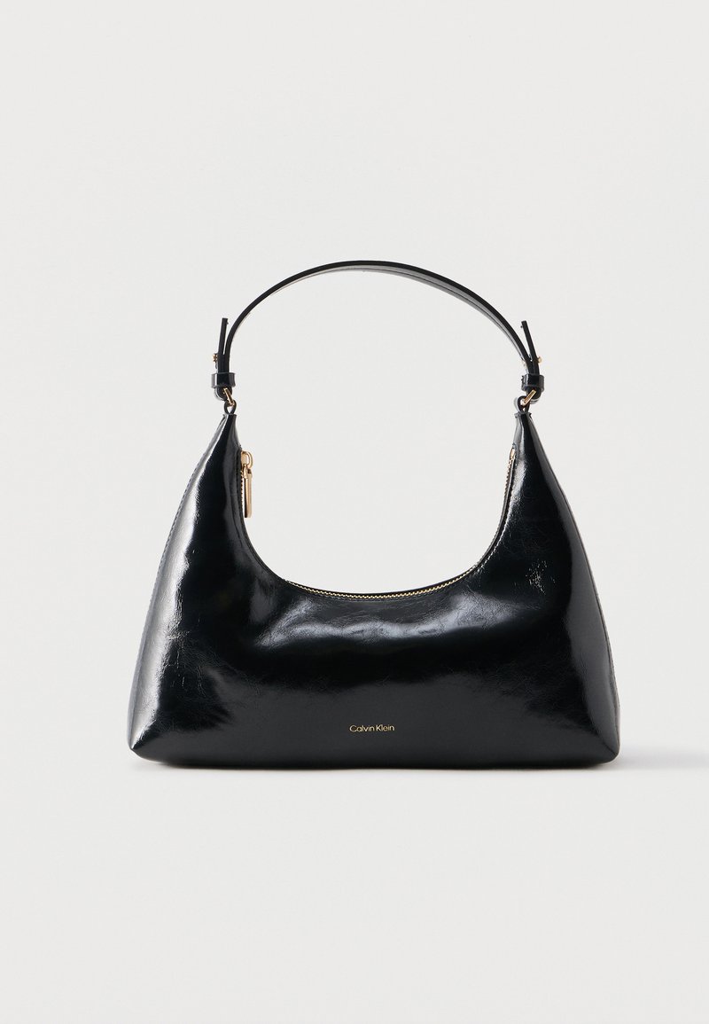 Μαύρη γυαλιστερή τσάντα Calvin Klein με χρυστό φερμουάρ και κοντό λουρί σε απλό λευκό φόντο.