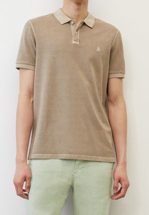 Polo beige à manches courtes avec deux boutons et logo brodé sur le côté gauche de la poitrine, porté avec un pantalon vert clair.