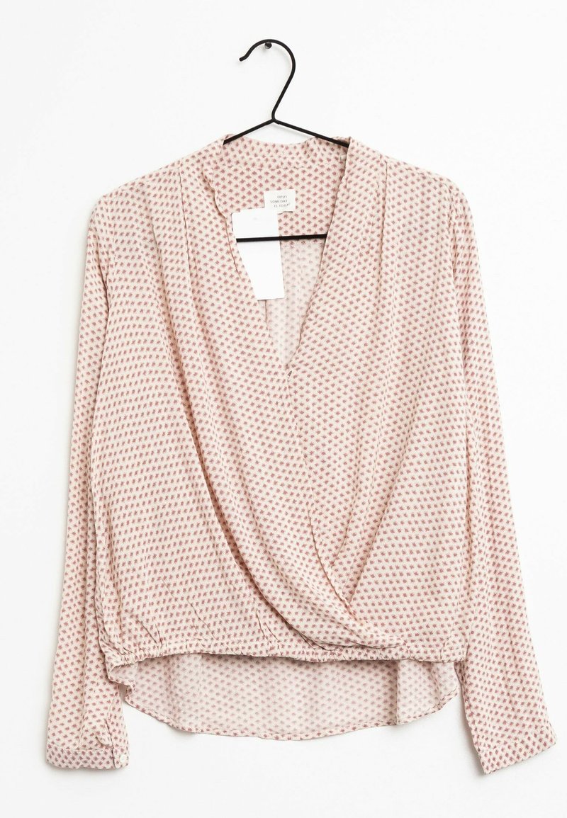 Blouse portefeuille à manches longues en rose clair avec de petits motifs géométriques rouges, dotée d'un col en V et d'un ourlet arrondi. Tissu lisse.