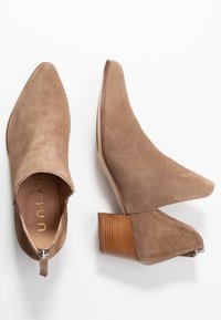 Tan suède enkellaarsjes met puntige neuzen, open zijkanten en een gestructureerde houten blokhak. Ritsdetail aan de achterkant van de hak.