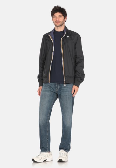 Giacca bomber leggera nera con zip frontale, fodera interna a contrasto, polsini ed elastico in vita, abbinata a jeans blu e sneakers bianche.