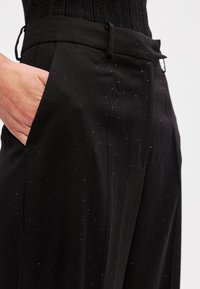 Melni bikses ar gludu audumu, izrotātas ar maziem, spīdīgiem sudraba punktiņiem. Pogas aizdare ar jostes cilpām un sānu kabatas detaļām. Pielāgota piegriezte.