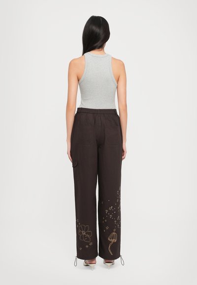 Gray ribbed tank top paired with loose-fitting, dark brown pants featuring floral and star embroidery near the cuffs and adjustable drawstrings.