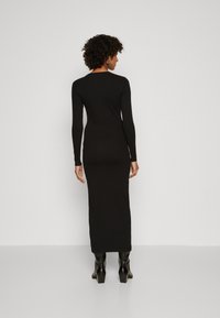 Black long-sleeve fitted dress with a round neckline, ankle-length design, and smooth texture, paired with black block-heeled boots.