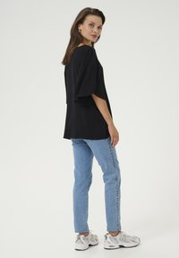 Czarna krótka bluzka z luźnym krojem, zestawiona z jasnoniebieskimi dżinsami i białymi trampkami; gładka tekstura, casualowy design.
