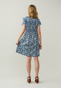 Modré šaty s potiskem, krátkými rukávy, nařaseným pasem a áčkovým střihem. Obsahují květinové vzory v různých odstínech modré a bílé.