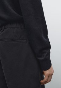 Marineblauwe trui met een zachte brei en zwarte broek met een elastische tailleband en een achterzak met een subtiele naaddetail.