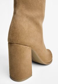 Beige mockasknäboot med en bred, klossig klack och en slät yta. Har en rund tå och en minimalistisk design.