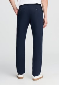 Pantaloni blu navy con una vestibilità dritta, realizzati in tessuto morbido. Presentano due tasche posteriori con bottoni e un orlo pulito alla caviglia.