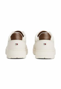 Beige Sneaker mit einem glatten Lederobermaterial, braunen Lederakzenten und strukturiertem Fersenbereich. Verfügt über einen gepolsterten Kragen und ein Logo-Patch auf der Rückseite.