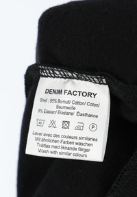 Black fabric with a care label; 95% cotton, 5% elastane; includes washing instructions in multiple languages and care symbols.
