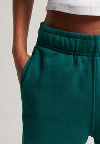 Grüne Baumwoll-Sweatpants mit elastischem Bund und Seitentaschen. Der Stoff hat ein weiches, strukturiertes Aussehen.