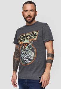 Camiseta de algodón gris con un estampado gráfico retro de Boba Fett y el texto "Star Wars: El Imperio Contraataca" en naranja y amarillo.