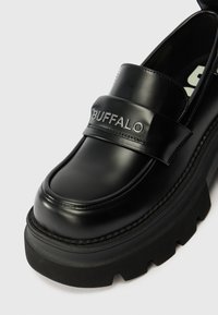 Loafer de couro preto com uma faixa larga apresentando "BUFFALO" em relevo, sola texturizada grossa, bico arredondado e detalhes de costura sutis.