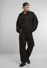 Fekete pamut dzseki két elülső zsebbel, fekete cargo nadrággal, amely lánc részletekkel van ellátva. Egyszerű fekete póló és csizma egészíti ki a megjelenést.