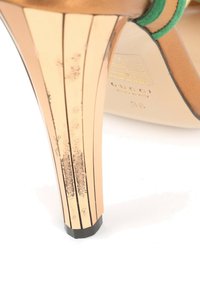 Gros plan d'une chaussure à talon haut avec talon métallique doré montrant des marques d'usure et une bride verte, marque Gucci fabriquée en Italie, taille 35.