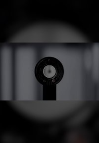 Schwarzes, rundes Gerät mit einem zentralen weißen Bereich, versehen mit Tasten und Anzeigen entlang des Randes, montiert auf einem vertikalen schwarzen Pfosten.