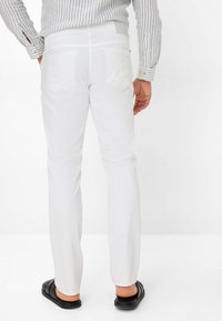 Weiße Jeanshose mit einer taillierten Passform, zwei Gesäßtaschen und glatter Textur. Kombiniert mit schwarzen Slipper-Sandalen.