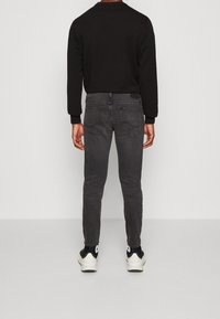 Jean slim gris foncé à taille mi-haute, design cinq poches avec des détails de couture subtils, associé à une chemise noire à manches longues.