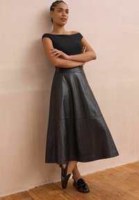 Top negro sin mangas combinado con una larga falda de cuero en forma de A. Textura suave, con costuras y una cintura ajustada. Zapatos negros completan el look.