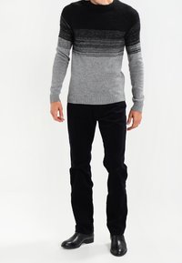 Pletený svetr v černé a šedé gradaci, kulatý výstřih, žebrované manžety, doplněný černými manšestrovými kalhotami a černými koženými botami.