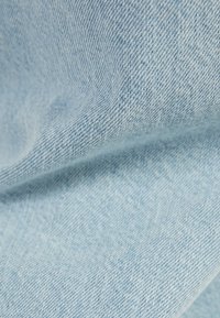 Tela de mezclilla azul claro con una superficie suave y texturizada. El patrón de tejido es visible, mostrando hilos finos y un brillo sutil.