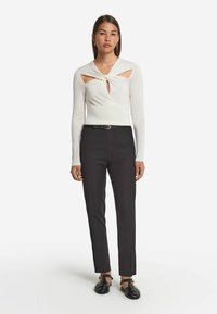 Vit långärmad topp med utskärningar och knut vid halsen, tillsammans med skräddarsydda svarta byxor och svarta remskor.