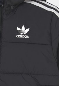 Chaqueta acolchada negra con el logo blanco de Adidas. Presenta franjas grises en los hombros. El material parece suave y con un ligero brillo. Cierre con cremallera.