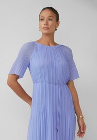 Helllila plissiertes Kleid mit kurzen Ärmeln, rundem Ausschnitt und tailliertem Gürtel. Glatte Textur und sanfte Drapierung.