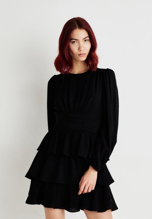 Sort lagdelt kjole med lange ærmer, samlet bærestykke og tekstureret stof. Har voluminøse lag og en tætsiddende talje for form.