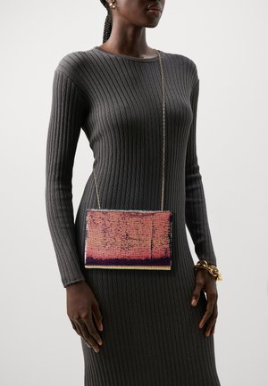 Kvinde iført en tætsiddende mørkegrå ribstrikket kjole, guldbøjler og en lille rektangulær pink paillet crossbody-taske med en tynd guldkæde.