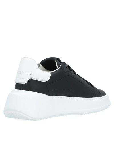Black leather sneaker with a white rubber sole, featuring a rounded shape, smooth texture, and a glossy heel tab with branding detail.
