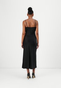 Black satin slip dress with spaghetti straps, knee-length, smooth texture, features a subtle back button detail, paired with black high heels.