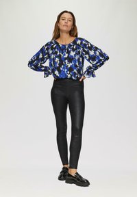 Blouse à motifs bleus et noirs avec des manches amples, associée à un legging noir moulant et brillant, accompagné de chaussures noires à semelles épaisses. Design simple et moderne.