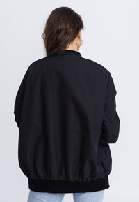 Schwarze Bomberjacke mit lockerer Passform, elastischen Bündchen und Saum sowie einer glatten Textur. Verfügt über einen hohen Kragen und seitliche Taschen.