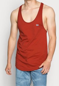 Camiseta sin mangas roja de algodón suave, con un escote redondeado y el logo "Lee" en el lado izquierdo del pecho. Combinada con jeans de color azul claro.