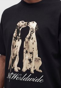 Due cani dalmata rivolti l'uno verso l'altro con i nasi che si toccano su una maglietta nera sopra un testo in corsivo con la scritta "Worldwide."