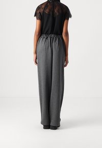Czarna bluzka z koronkowym detalem oraz szare plisowane spodnie o szerokich nogawkach. Spodnie posiadają elastyczną talię i gładką fakturę.