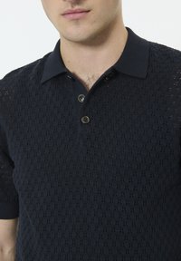 Polo en tricot bleu marine avec un motif texturé, manches courtes et col classique. Deux boutons au niveau du col.