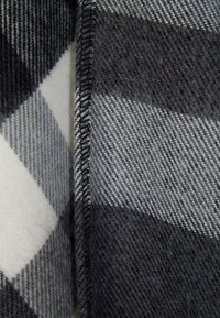 Gros plan d'un tissu à carreaux noir, gris et blanc avec une couture visible le long du pli.