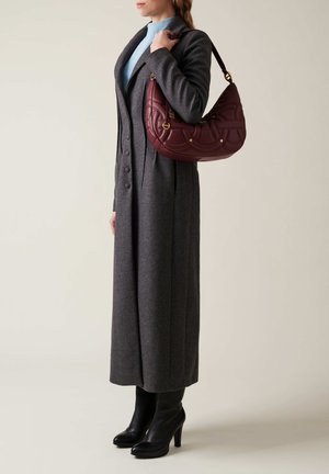 Manteau en laine gris avec des boutons, associé à un col roulé bleu clair. Tenant un sac en cuir bordeaux avec un design matelassé et des accents dorés. Bottes à talons noires.