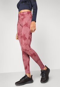 Legíny s červeným vzorom tie-dye, vyrobené z pružnej látky. Kombinované s čiernymi textúrovanými teniskami so šnurovaním.