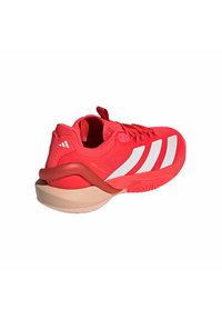 Scarpa atletica rossa con tomaia in rete, tre strisce bianche, colletto imbottito e una suola in gomma beige spessa e testurizzata. Passante sul tallone.