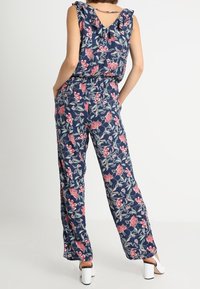 Marinblå blommig jumpsuit med volangärmar, elastisk midja och vida ben, prydd med rosa och gröna blommönster.